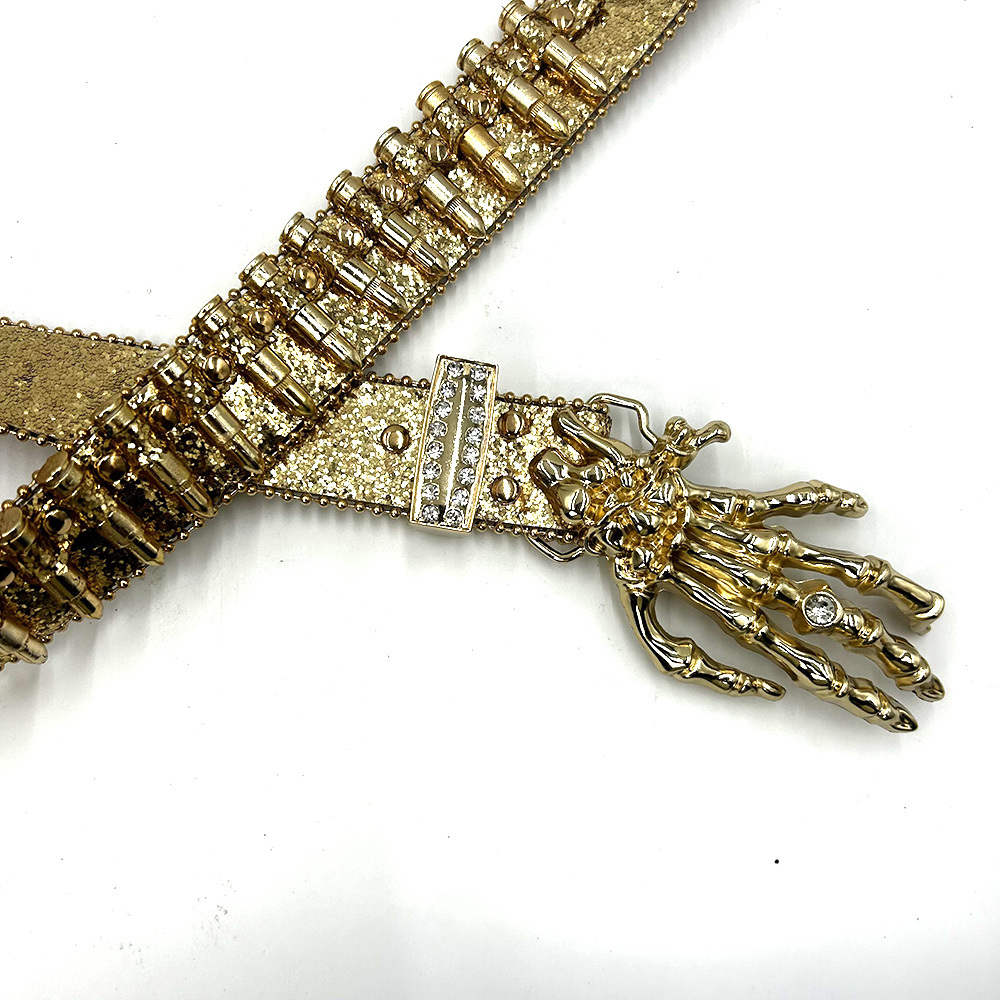 Close-up of gold skeleton-hand belt buckle and bullet-inspired glitter strap